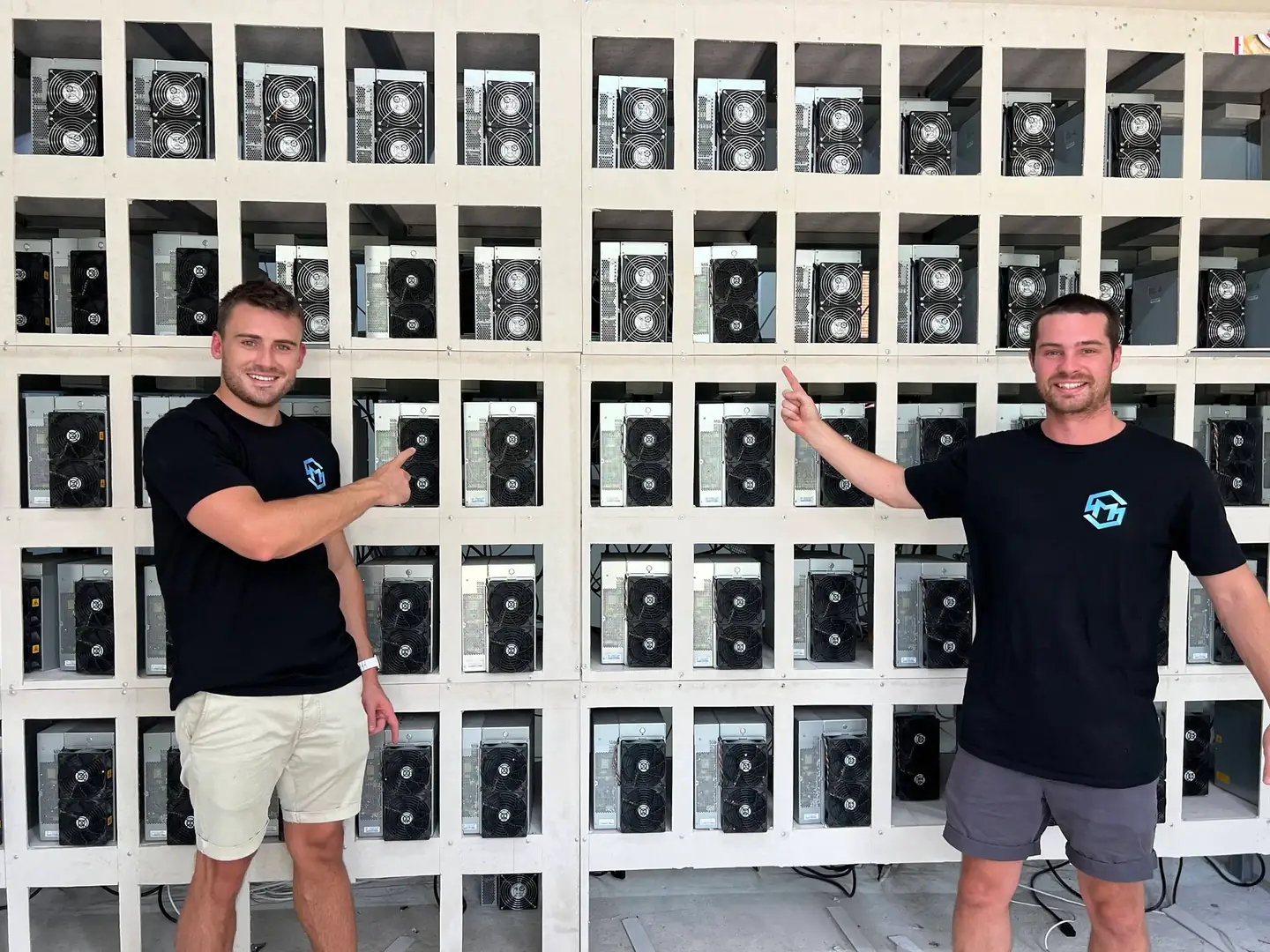 William Wright and Callum Cameron pointing at a wall of racked miners