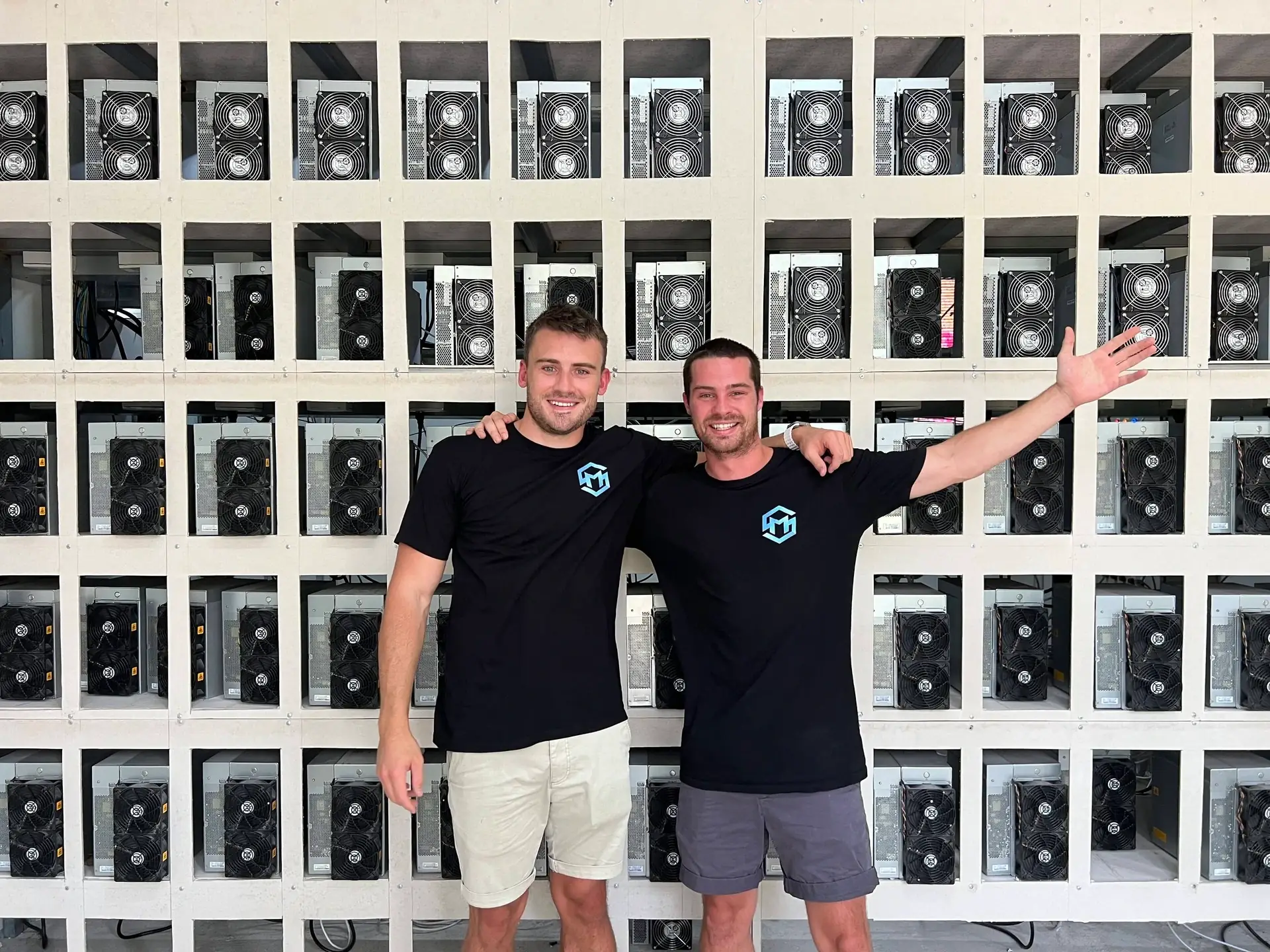 Two Mining Store team members in front of a wall of racked Bitcoin miners
